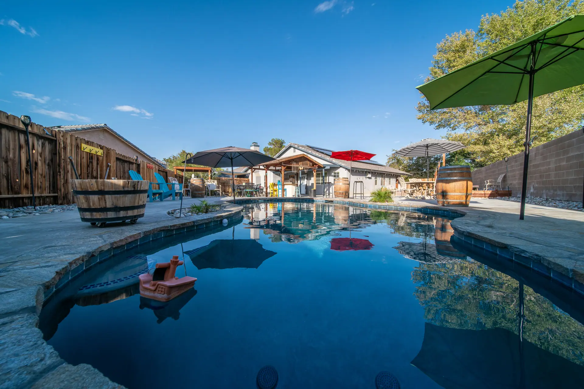 Backyard freeform pool with flagstone edging, patio umbrellas and a block wall under a clear blue sky